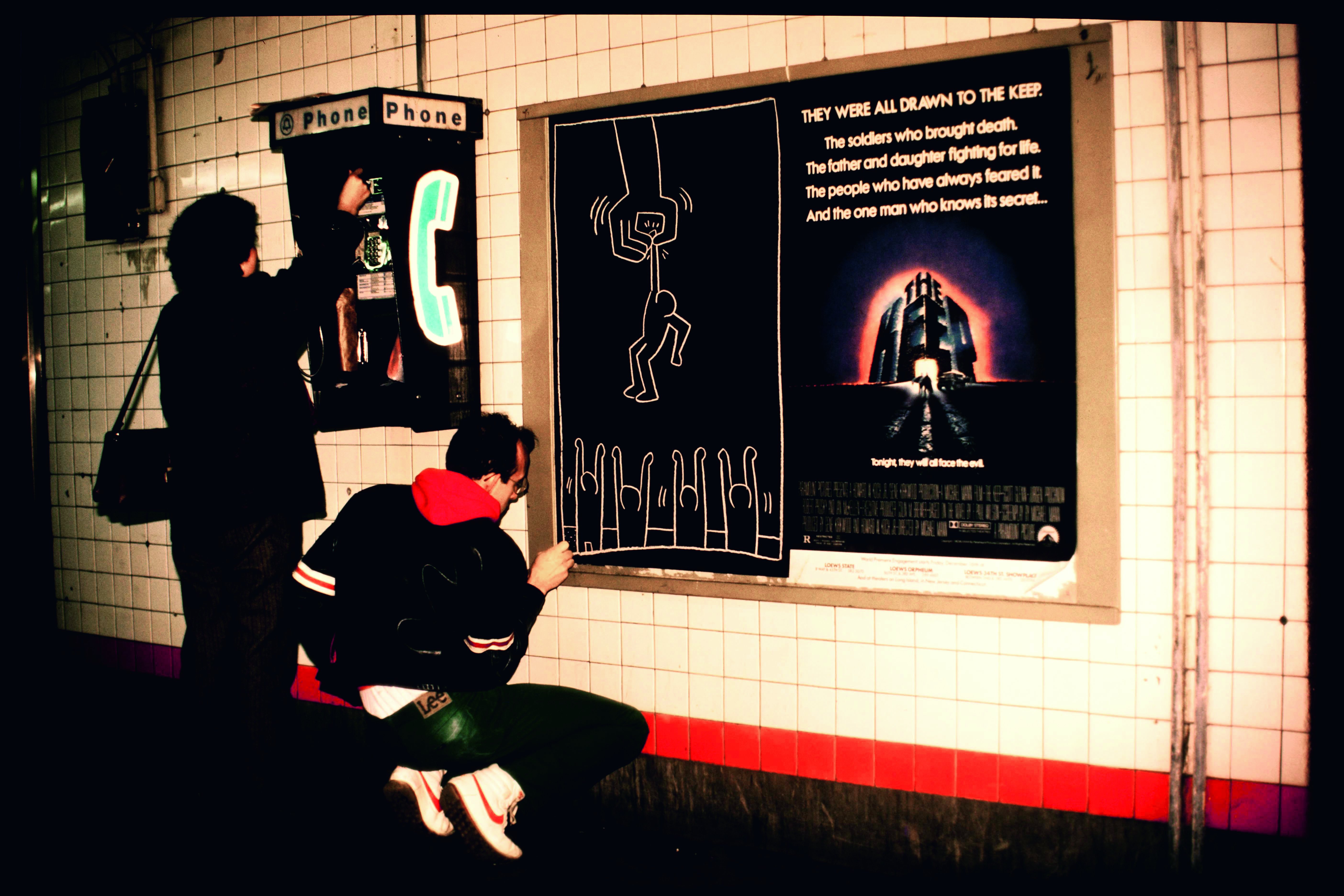 Keith Haring tekent in een metrostation, New York, 1984. Foto: Tseng Kwong Chi ©Keith Haring Foundation Lightbox_Tseng_Haring_KH_woman_phonebooth.jpg