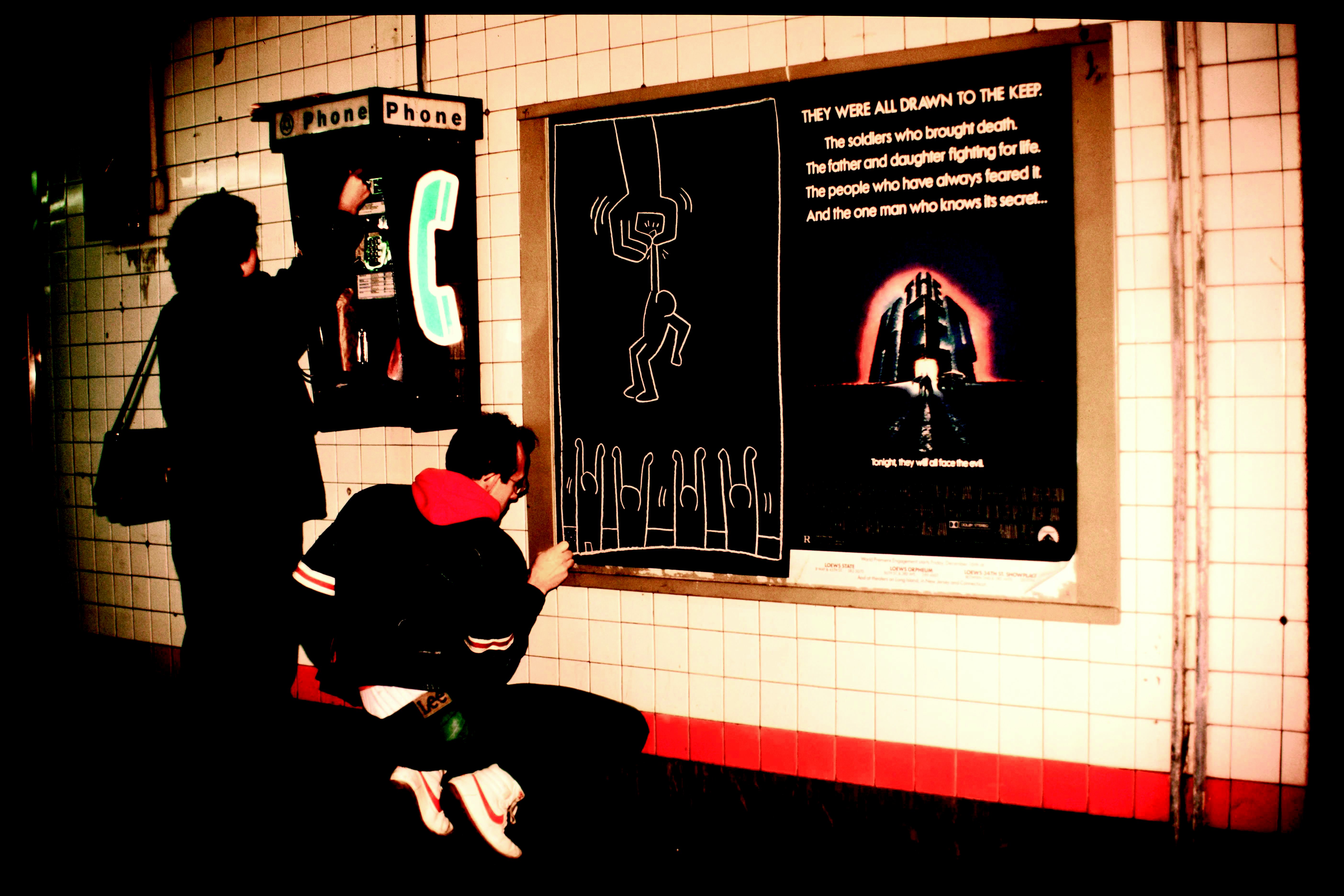 Keith Haring tekent in een metrostation, New York, 1984. Foto: Tseng Kwong Chi ©Keith Haring Foundation Lightbox_Tseng_Haring_KH_woman_phonebooth.jpg